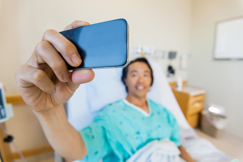 7703273-male-patient-taking-self-portrait-through-mobile-phone-in-hospit